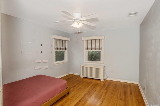 unfurnished bedroom with radiator, ceiling fan, billiards, and light wood-type flooring