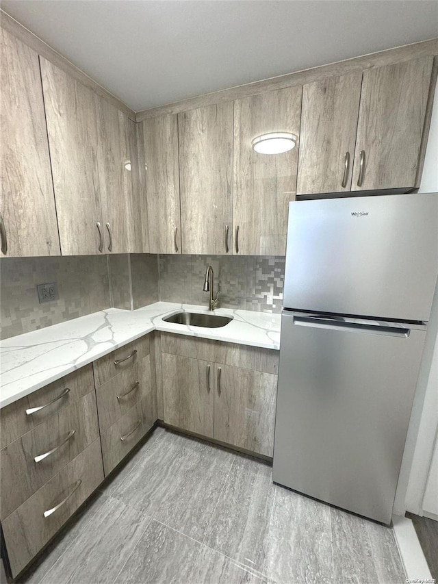 kitchen featuring backsplash, stainless steel refrigerator, light stone counters, and sink