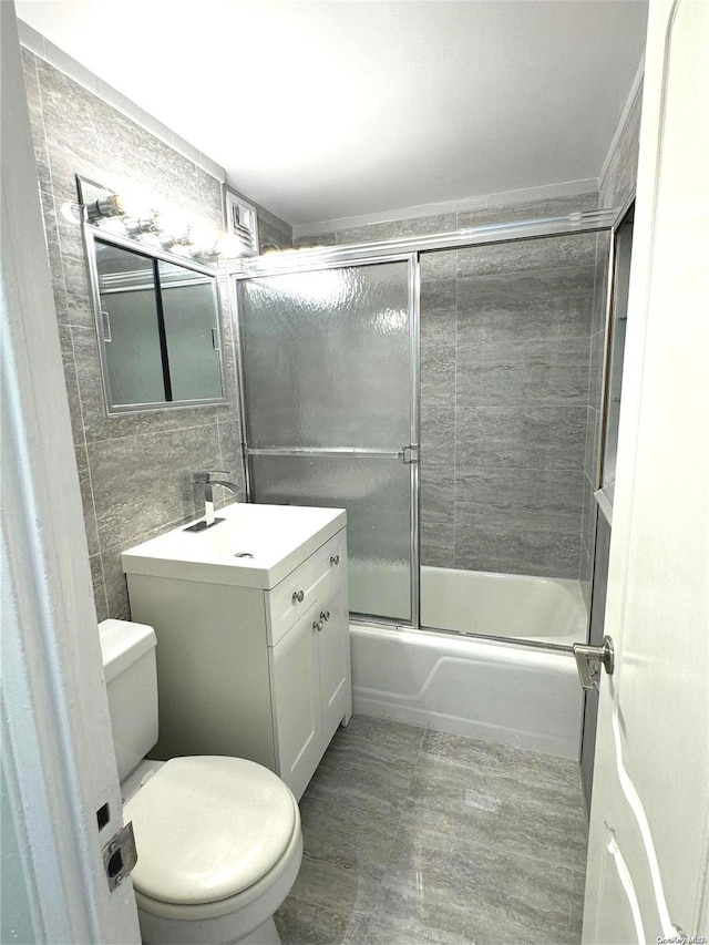 full bathroom with vanity, toilet, tile walls, and bath / shower combo with glass door