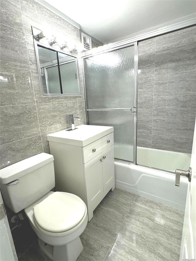 full bathroom featuring shower / bath combination with glass door, vanity, tile walls, and toilet