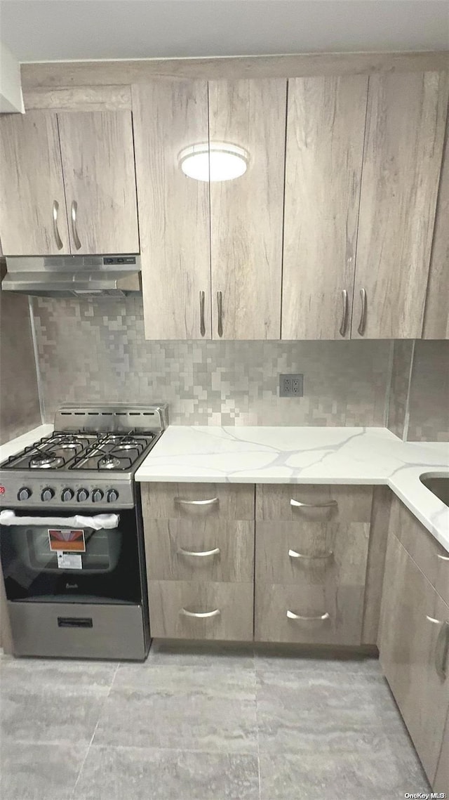 kitchen with light stone countertops, gas range, decorative backsplash, and light brown cabinetry