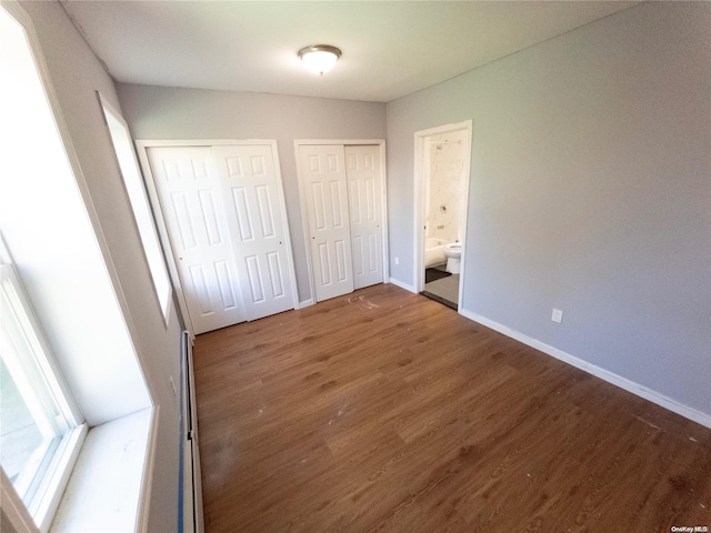 unfurnished bedroom with two closets, ensuite bath, and dark hardwood / wood-style floors