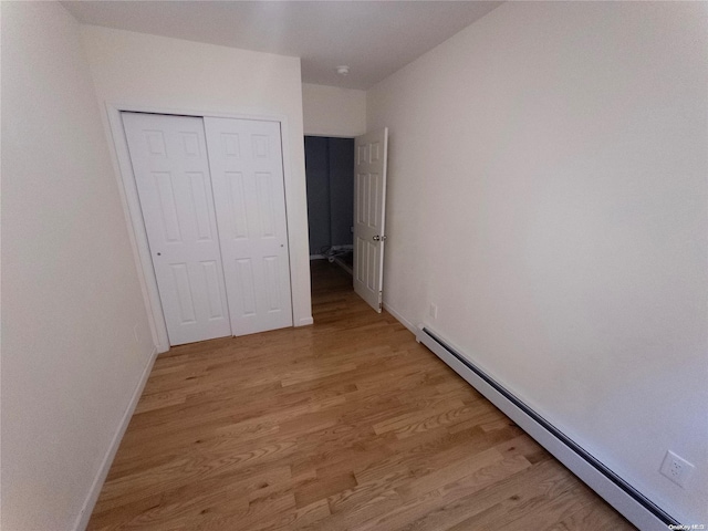 unfurnished bedroom with baseboard heating, a closet, and light hardwood / wood-style flooring