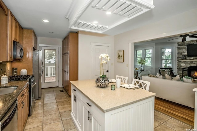 9 N Bayles Ave, Port Washington, NY 11050 - kitchen with a stone fireplace, white cabinets, light hardwood / wood-style flooring, a kitchen island, and appliances with stainless steel finishes