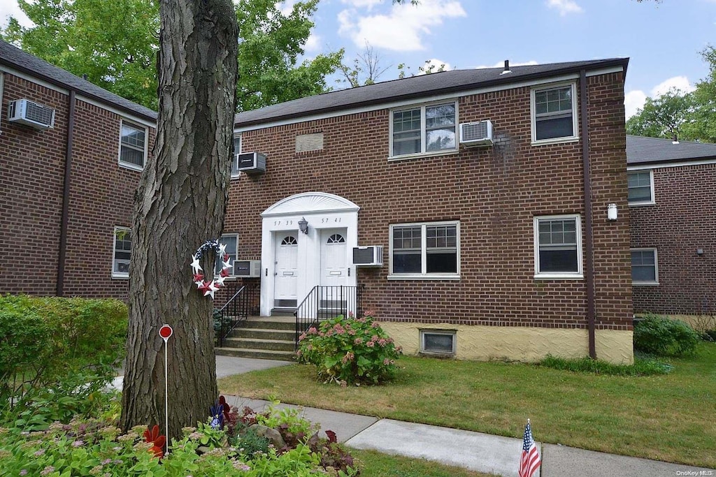 view of front of home with an AC wall unit and a front lawn