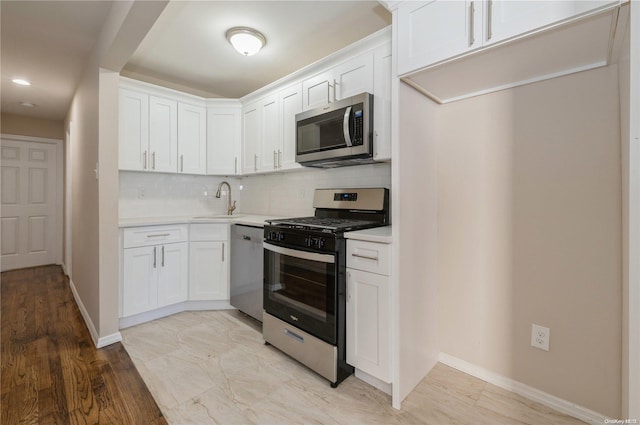 kitchen featuring sink, light hardwood / wood-style floors, decorative backsplash, white cabinets, and appliances with stainless steel finishes