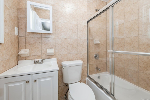 full bathroom with vanity, bath / shower combo with glass door, tile walls, and toilet