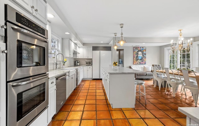 kitchen with tasteful backsplash, stainless steel appliances, a kitchen island, a notable chandelier, and white cabinetry