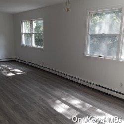 empty room featuring wood-type flooring and a baseboard heating unit