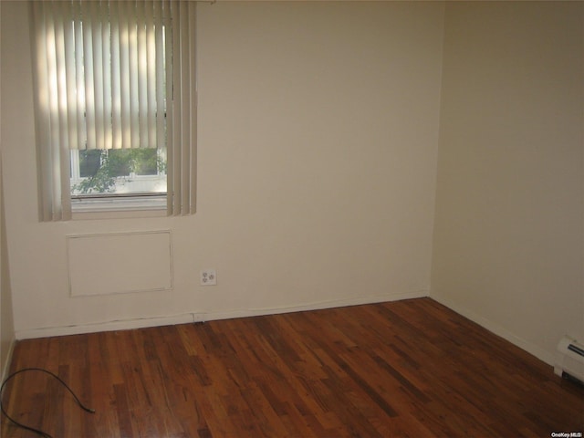 empty room featuring baseboard heating and dark wood-type flooring