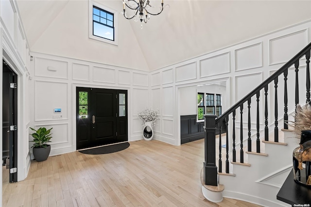 entrance foyer featuring a towering ceiling, stairway, light wood-type flooring, a chandelier, and a decorative wall