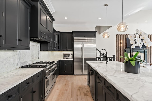 kitchen with a sink, dark cabinets, premium appliances, and light stone countertops