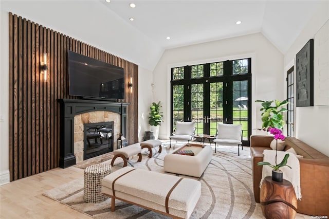 living area featuring lofted ceiling, french doors, a stone fireplace, and wood finished floors