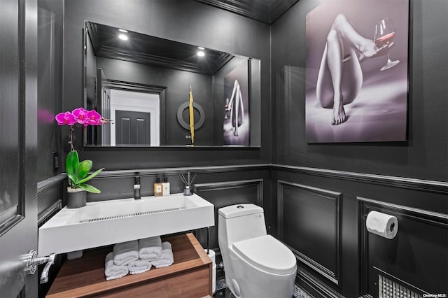 bathroom with toilet, a sink, a decorative wall, and crown molding