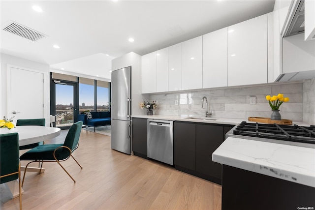 kitchen featuring decorative backsplash, appliances with stainless steel finishes, sink, light hardwood / wood-style floors, and white cabinetry