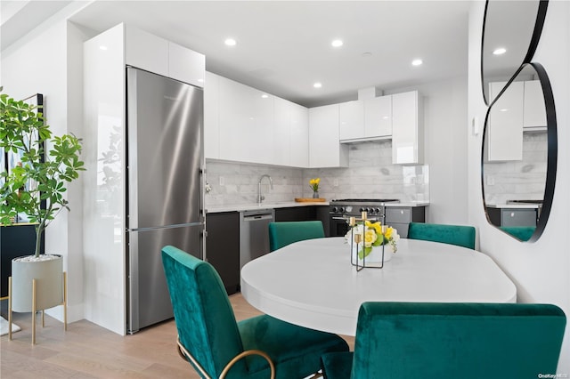 kitchen featuring backsplash, high end appliances, sink, white cabinets, and light hardwood / wood-style floors