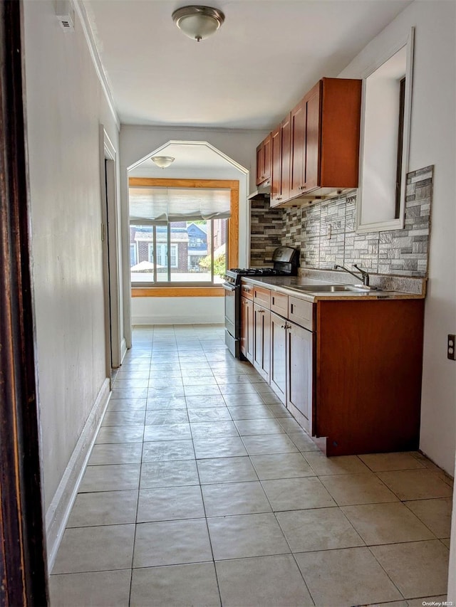 kitchen with light tile patterned floors, tasteful backsplash, stainless steel gas range oven, and sink