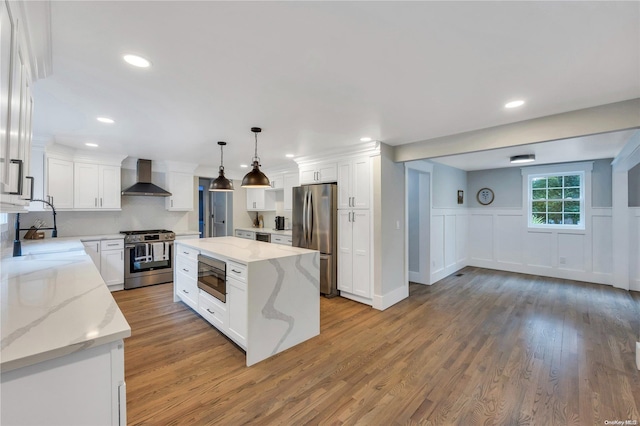 kitchen featuring wall chimney exhaust hood, appliances with stainless steel finishes, decorative light fixtures, a kitchen island, and white cabinetry