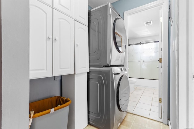 laundry room with cabinets, light tile patterned floors, and stacked washer and dryer