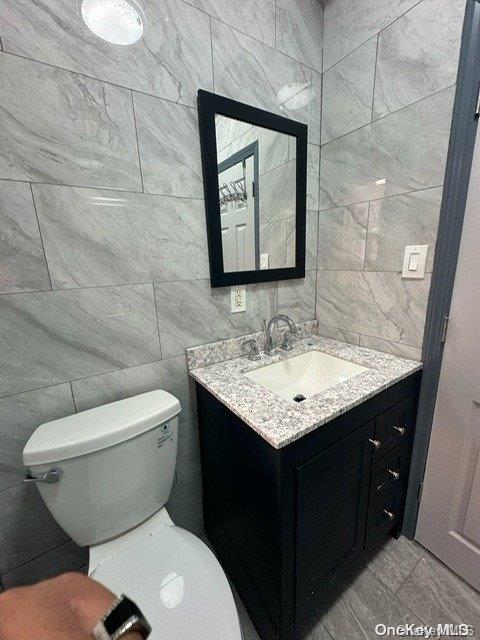 bathroom featuring vanity, toilet, and tile walls