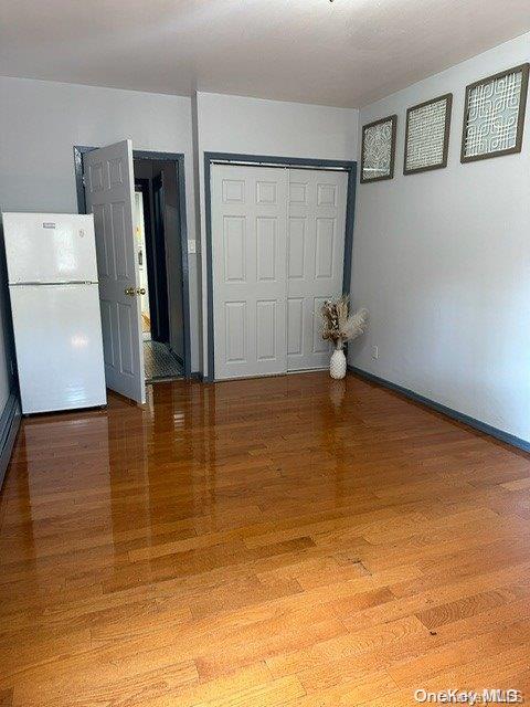 unfurnished bedroom featuring hardwood / wood-style floors, white refrigerator, and a closet