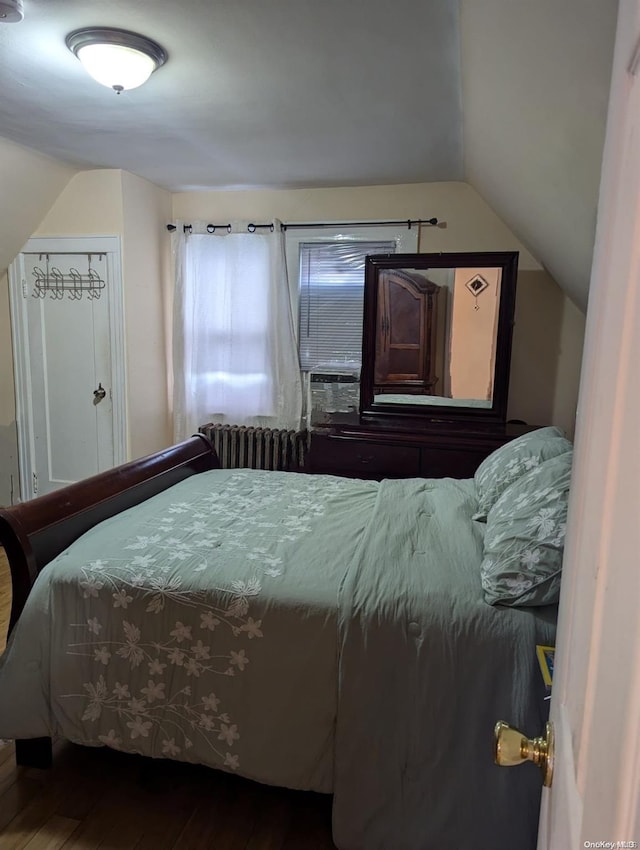 bedroom with hardwood / wood-style floors, radiator heating unit, and vaulted ceiling