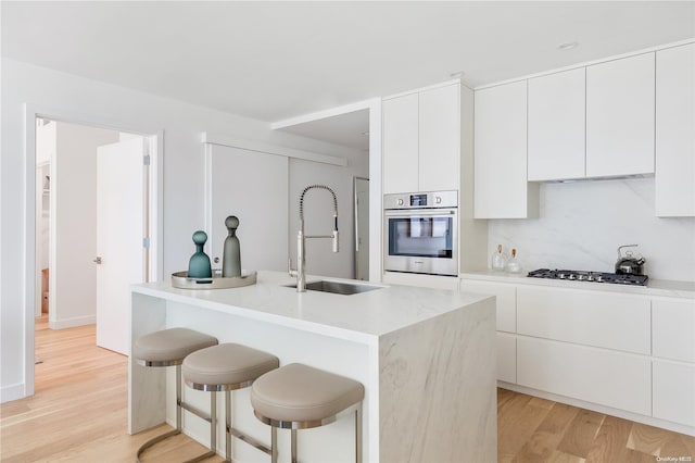 kitchen with sink, appliances with stainless steel finishes, an island with sink, white cabinets, and light wood-type flooring