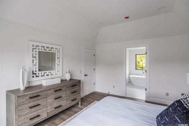 bedroom with connected bathroom, dark wood-type flooring, and vaulted ceiling