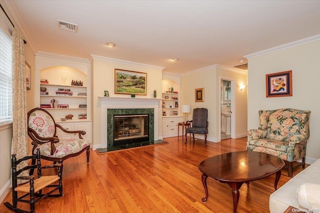 living area with a premium fireplace, built in features, wood-type flooring, and ornamental molding