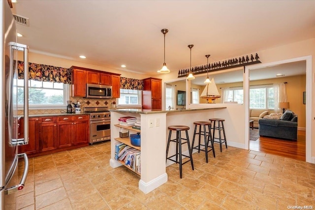 kitchen with a breakfast bar, decorative backsplash, appliances with stainless steel finishes, decorative light fixtures, and kitchen peninsula