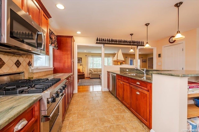 kitchen featuring light stone countertops, sink, backsplash, decorative light fixtures, and appliances with stainless steel finishes