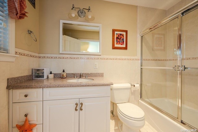 full bathroom featuring vanity, bath / shower combo with glass door, tile walls, and toilet