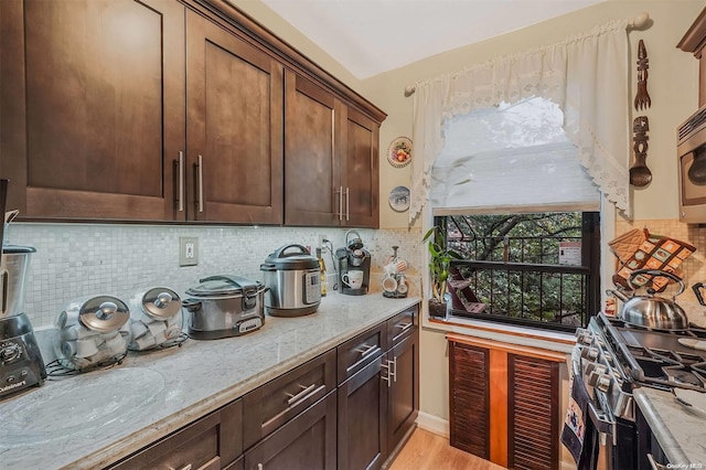 kitchen featuring appliances with stainless steel finishes, light wood-type flooring, tasteful backsplash, and light stone counters