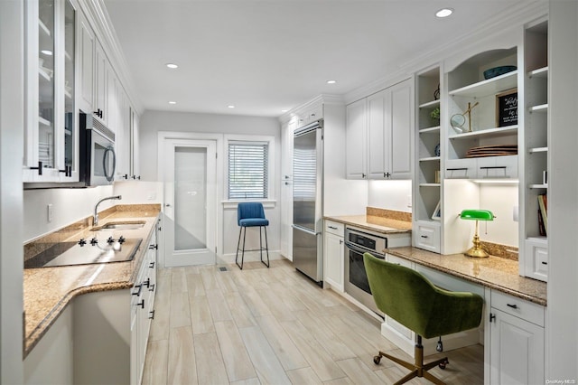 kitchen with sink, light wood-type flooring, appliances with stainless steel finishes, light stone countertops, and white cabinets