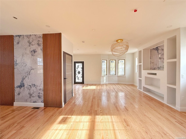 unfurnished living room with built in shelves, light wood-type flooring, and an inviting chandelier