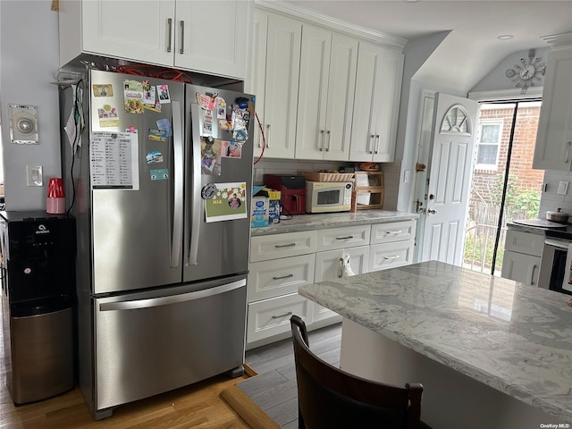 kitchen featuring stainless steel refrigerator, light stone counters, and white cabinets