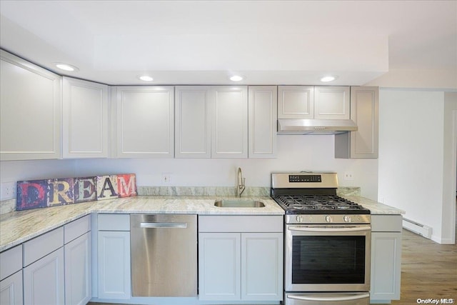 kitchen featuring appliances with stainless steel finishes, light stone counters, sink, wood-type flooring, and a baseboard radiator