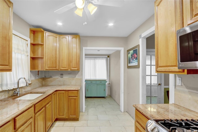 kitchen featuring stainless steel appliances, light stone counters, ceiling fan, and sink