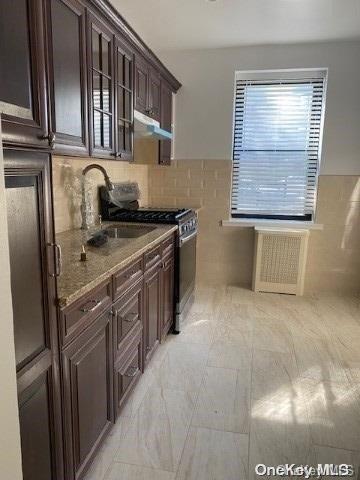 kitchen featuring light stone countertops, tasteful backsplash, dark brown cabinetry, sink, and stainless steel gas stove