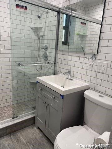 bathroom with decorative backsplash, walk in shower, vanity, hardwood / wood-style flooring, and toilet