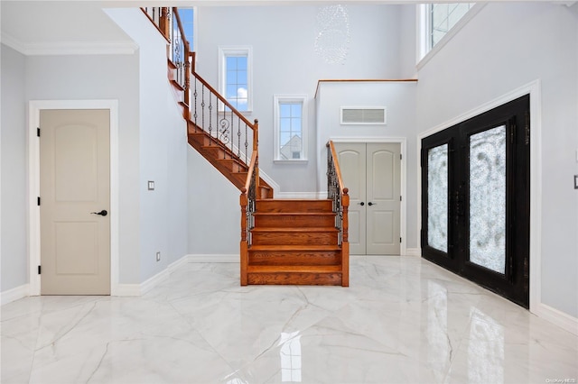 entryway featuring a notable chandelier, a towering ceiling, crown molding, and french doors