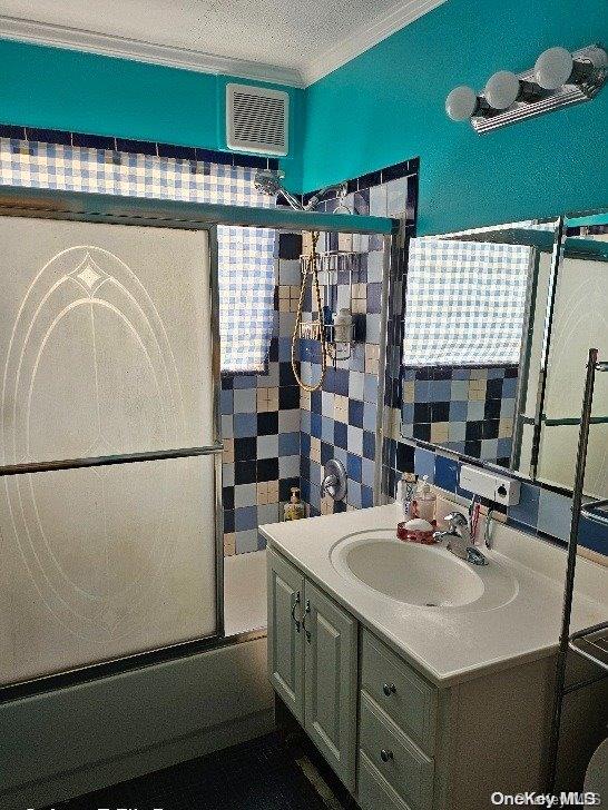 bathroom featuring vanity, bath / shower combo with glass door, a textured ceiling, and ornamental molding