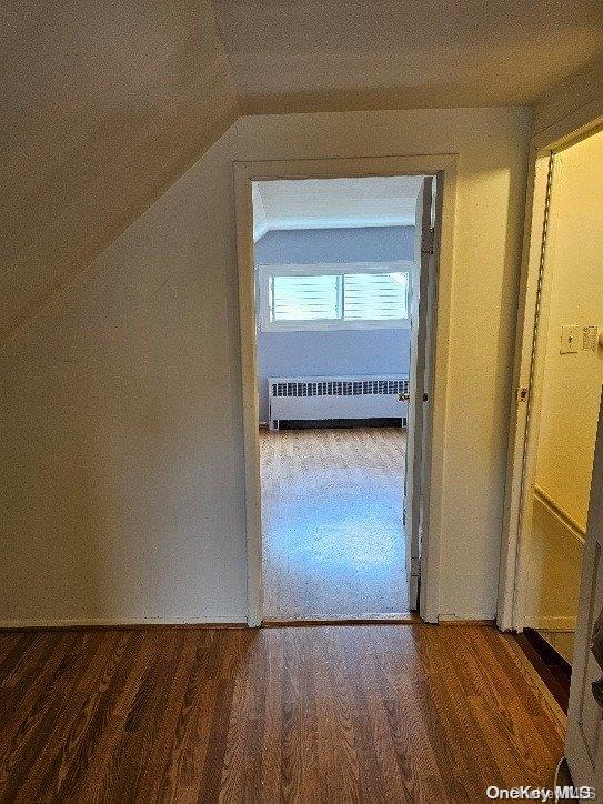 additional living space with radiator, dark hardwood / wood-style floors, and lofted ceiling