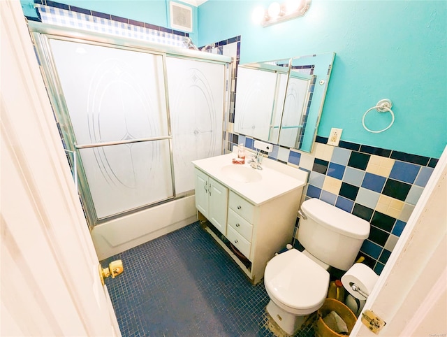 full bathroom with enclosed tub / shower combo, tile patterned floors, toilet, vanity, and tile walls