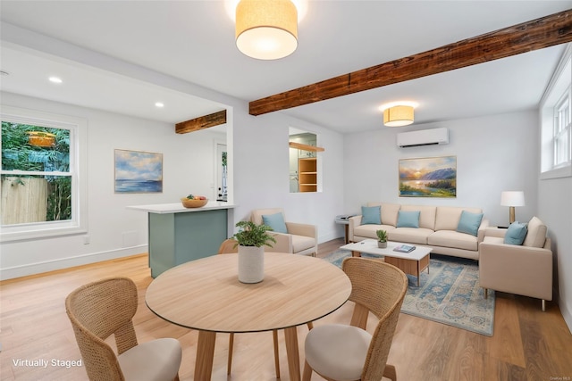 dining space featuring beam ceiling, a wall mounted AC, and light hardwood / wood-style flooring