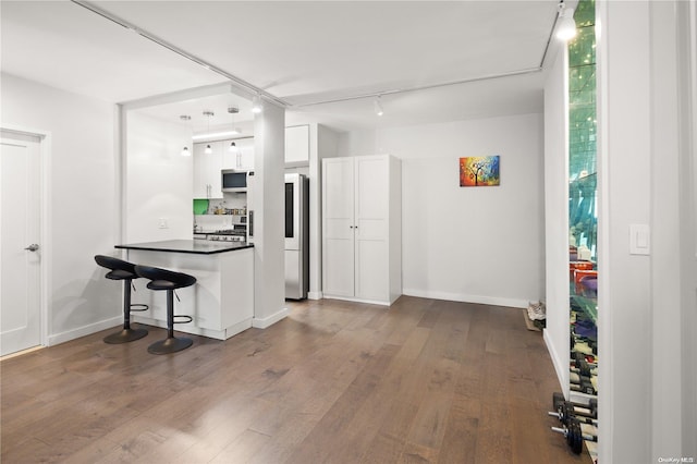 kitchen with dark wood-type flooring, track lighting, appliances with stainless steel finishes, a kitchen bar, and white cabinetry