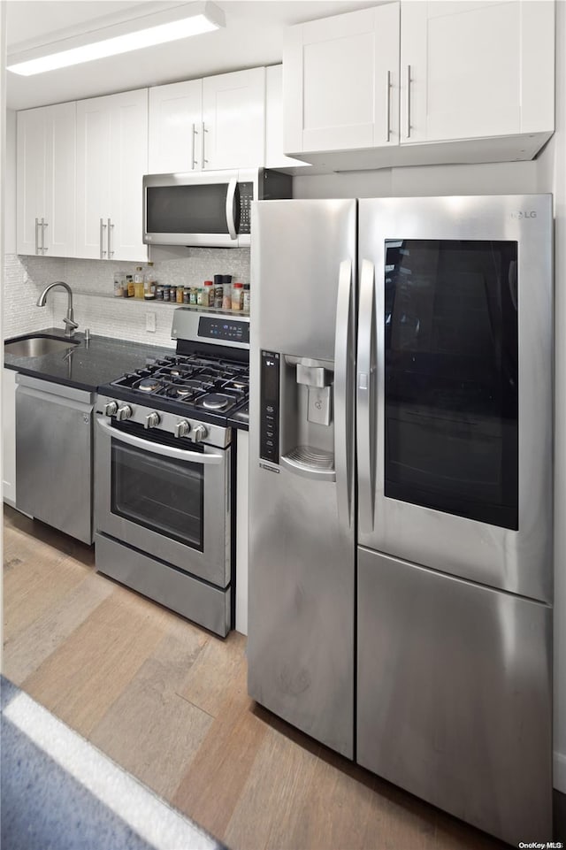 kitchen with sink, tasteful backsplash, appliances with stainless steel finishes, white cabinets, and light wood-type flooring