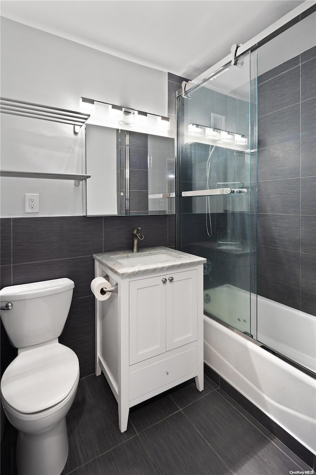 full bathroom with combined bath / shower with glass door, tile patterned floors, vanity, tile walls, and toilet