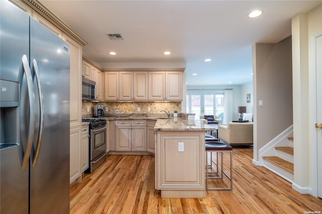 kitchen featuring a kitchen breakfast bar, light stone counters, light hardwood / wood-style floors, and appliances with stainless steel finishes