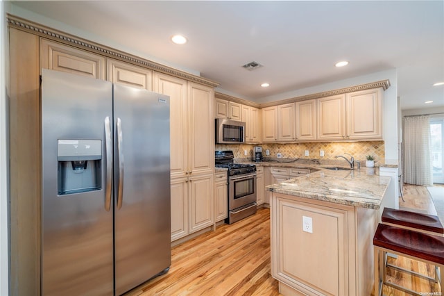 kitchen featuring a breakfast bar area, light hardwood / wood-style flooring, light stone countertops, kitchen peninsula, and stainless steel appliances